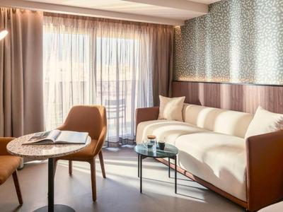 Sala luminosa con sofá, sillón y mesa junto a una gran ventana con cortina.