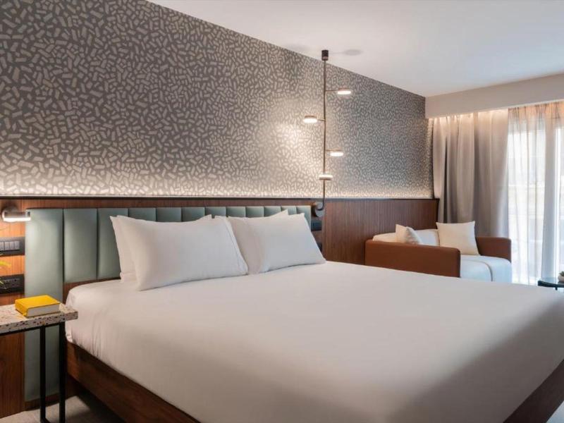 Habitación de hotel moderna con cama grande, área de sofá y suelo alfombrado.