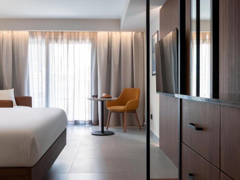 Habitación de hotel moderna con cama grande, sillón y ventana con cortinas.