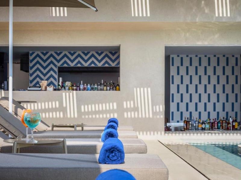 Zona de piscina con tumbonas, toallas azules y bar con paredes decoradas al fondo.
