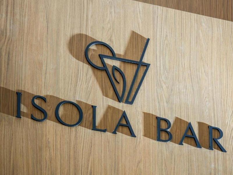 Logotipo negro y letrero 'ISOLA BAR' en una pared de madera clara.