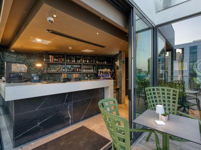 Moderner Hotelbarbereich mit schwarzem Marmortresen und grünen Stühlen auf der Terrasse.