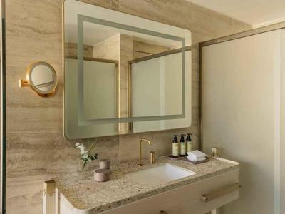 Moderní koupelna s velkým zrcadlem, umyvadlem a elegantním nástěnným osvětlením.