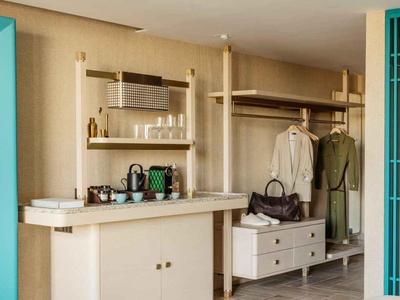 Koutek s šatní skříní, zrcadlem, pověšeným oblečením, taškami a pracovní plochou v hotelovém pokoji.