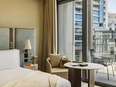 Moderní hotelový pokoj s postelí, křeslem, stolem a balkonem s výhledem na město.