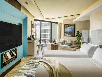 Moderně zařízený hotelový pokoj s manželskou postelí, pohovkou a televizí na zdi.