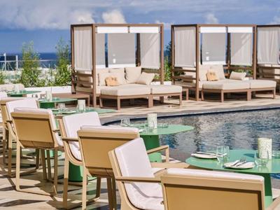 Area piscina con comode sedie a sdraio e divani sotto tendalini bianchi.