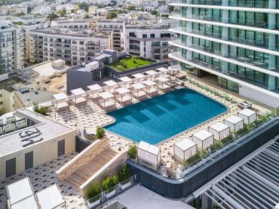 Piscina moderna sul tetto di un hotel con lettini e ombrelloni in ambiente urbano.