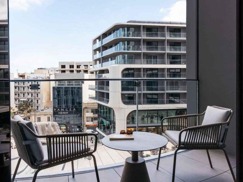 Balkon se dvěma židlemi a stolem, pohled na moderní městské bytové domy.