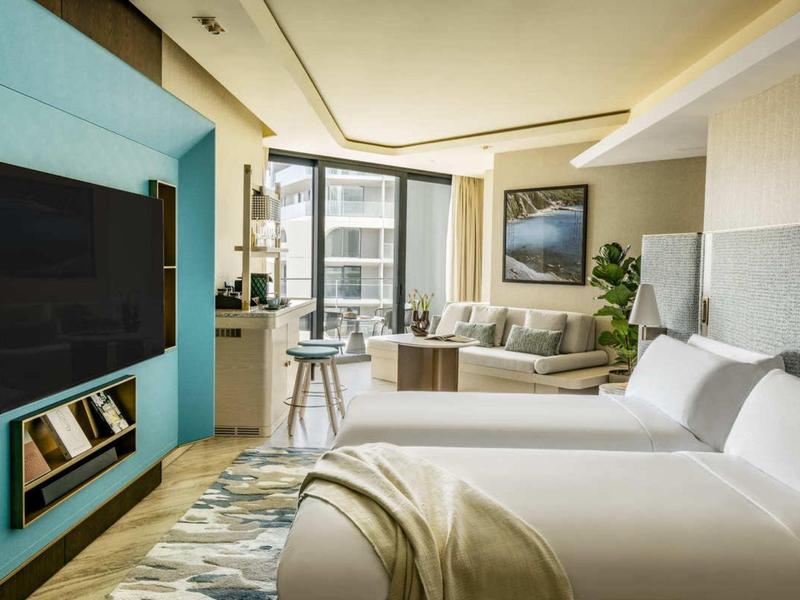 Moderně zařízený hotelový pokoj s manželskou postelí, pohovkou a televizí na zdi.