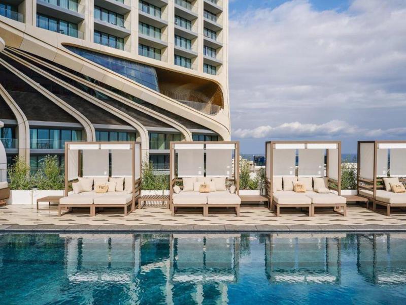 Luxusní bazén s lehátky a velkými slunečníky před moderním hotelem.