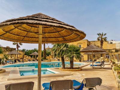 Hotelpoolbereich mit Sonnenschirmen, Liegestühlen und Palmen unter klarem Himmel.