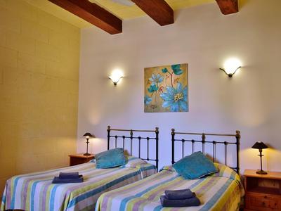 Pokoj se dvěma jednolůžky, dřevěnými trámy, nočními stolky a nástěnnými lampami.