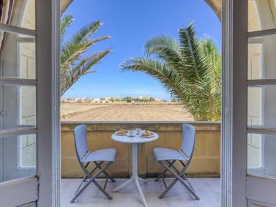 Balkon mit kleinem runden Tisch und zwei Stühlen mit Blick auf Palmen und Meer.