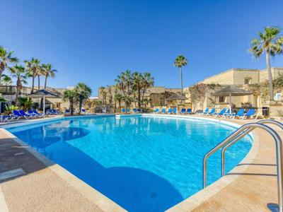 Großer Pool mit Liegestühlen und Palmen unter klarem blauem Himmel in einem Resort.