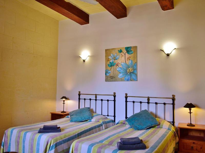 Pokoj se dvěma jednolůžky, dřevěnými trámy, nočními stolky a nástěnnými lampami.