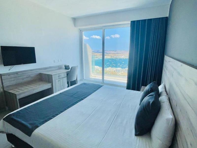 Habitación de hotel moderna con cama grande y vista al mar a través de ventanas de suelo a techo.