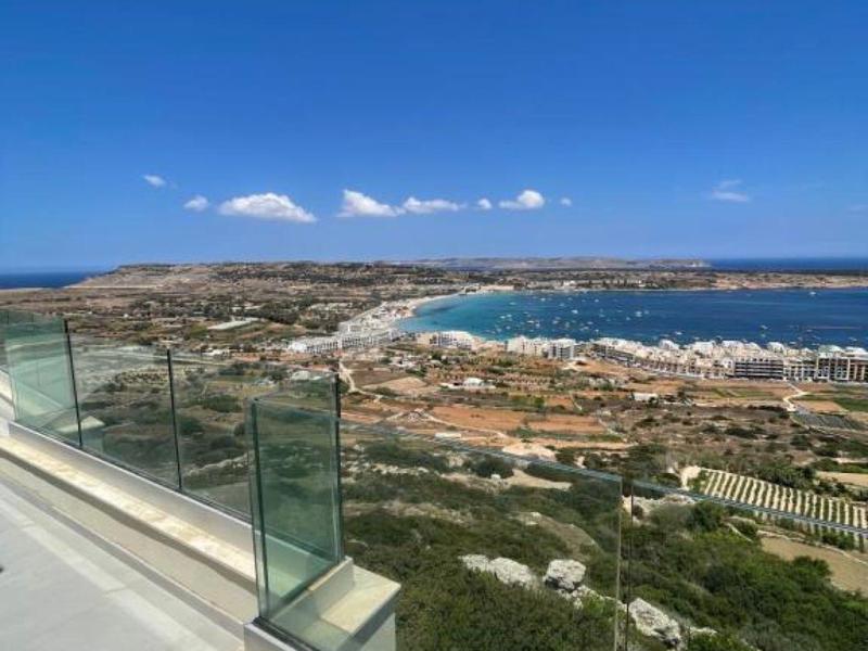 Vista de una ciudad costera con playa, mar y cielo azul desde una barandilla de vidrio.