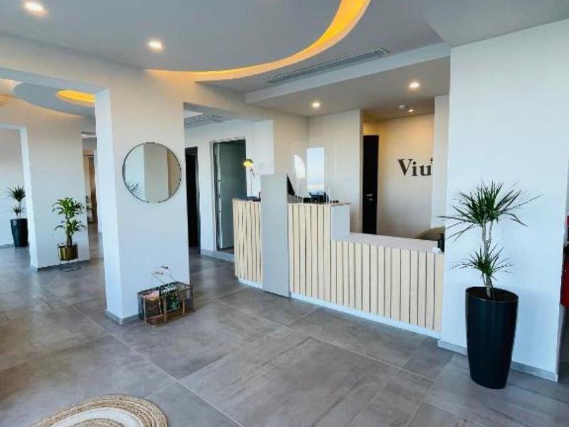 Recepción de hotel moderna con iluminación curva en el techo y plantas en macetas grandes.