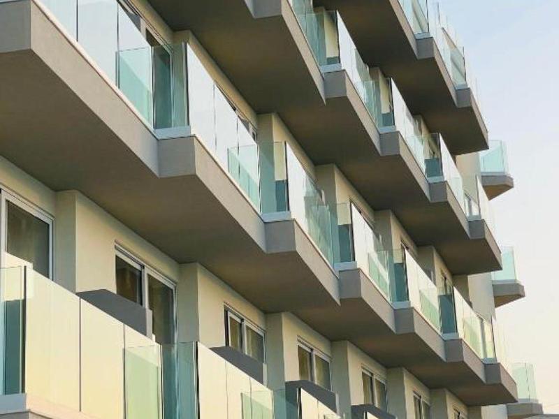 Fachada de un hotel con varios balcones y barandillas de vidrio a la luz del día.