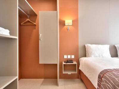 Hoek van hotelkamer met bed, nachtkastje, kledingkast en perzikkleurige accentmuur.