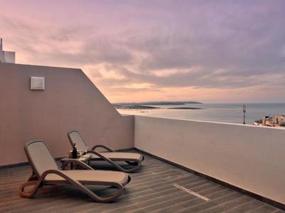 Twee ligstoelen op een terras met uitzicht op een rustige zee bij zonsondergang.