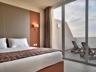 Moderne hotelkamer met groot bed en schuifdeur naar balkon met ligstoelen.