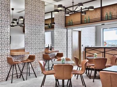 Nowoczesna restauracja z wzorzystymi kolumnami, wygodnymi brązowymi krzesłami i dużym oknem z widokiem na zewnątrz.