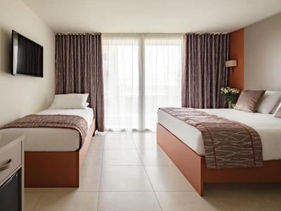 Hotelkamer met tweepersoonsbed en eenpersoonsbed, tv, gordijnen en neutrale tinten.