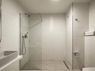 Moderne hotelbadkamer met witte tegels, glazen douche, wastafel en netjes gerangschikte handdoeken.