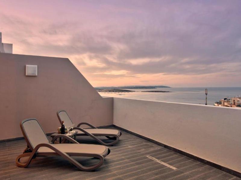 Twee ligstoelen op een terras met uitzicht op een rustige zee bij zonsondergang.