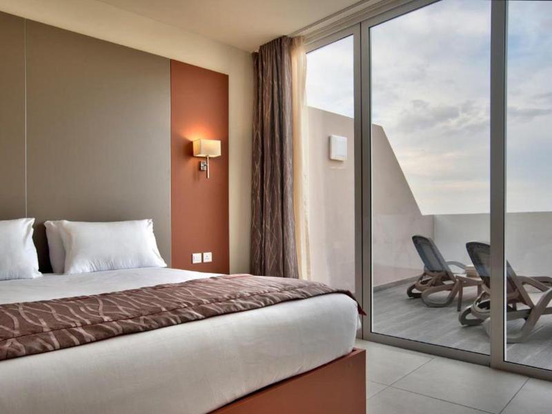 Moderne hotelkamer met groot bed en schuifdeur naar balkon met ligstoelen.