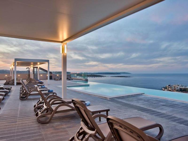 Gezellige ligstoelen langs een zwembad op het dak met uitzicht op de oceaan onder een bewolkte hemel.