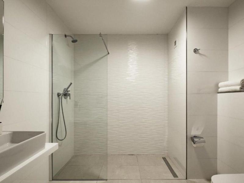 Moderne hotelbadkamer met witte tegels, glazen douche, wastafel en netjes gerangschikte handdoeken.