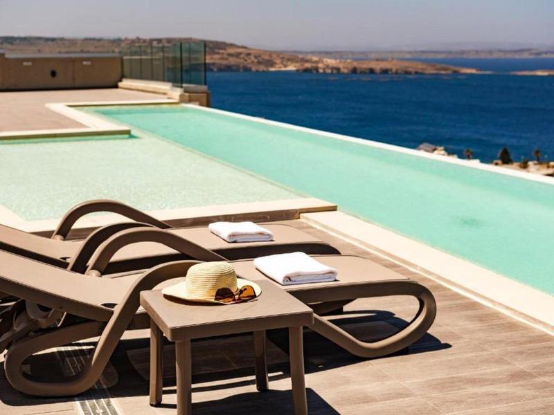 Ligbedden met handdoeken en een drankje aan een infinity zwembad met uitzicht op zee.