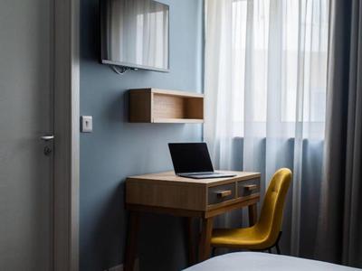 Helles Zimmer mit Schreibtisch, Laptop und gelbem Stuhl neben einem großen Fenster.