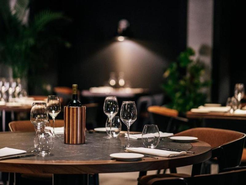 Elegantes Restaurant mit gedeckten Tischen, Weingläsern und gedämpfter Beleuchtung.