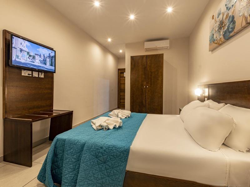 Camera d'hotel moderna con letto matrimoniale, TV a parete e armadio in colori caldi.