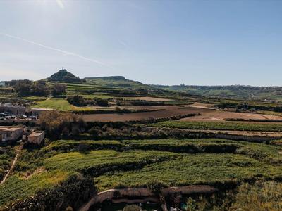 Groene velden en heuvels onder een heldere lucht met een dorp aan de linkerkant.