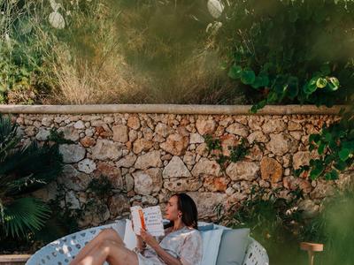 Frau entspannt sich auf einem runden Lounge-Sessel im Garten vor einer Steinmauer.