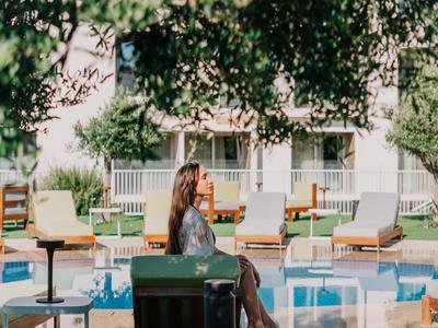 Frau entspannt am Pool in einem Garten mit Sitzgelegenheiten und Sonnenschirmen.