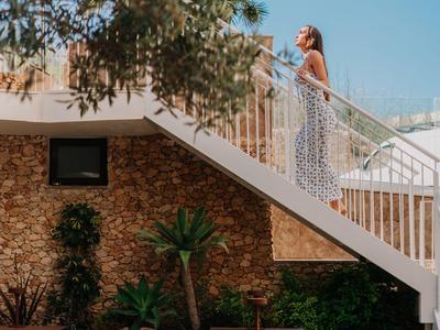 Frau im weißen Kleid geht eine Außentreppe in einer sonnigen Gartenanlage hoch.