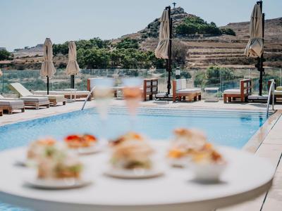 Poolbereich mit Sonnenliegen und Blick auf Hügel und Wasser im Hintergrund