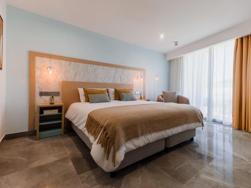 Moderne hotelkamer met groot bed, natuurlijk licht en lichte gordijnen.