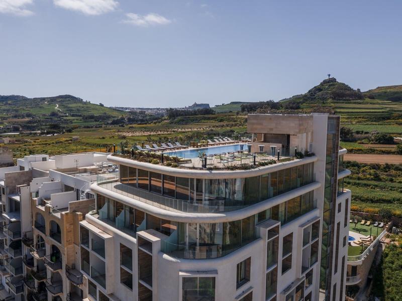 Modern hotelgebouw met dakterras en zwembad in een landelijke omgeving.