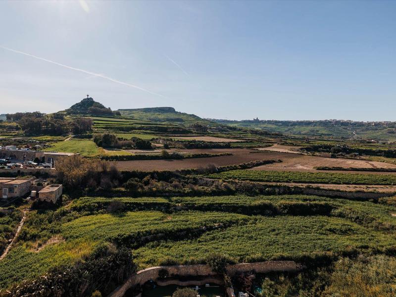 Groene velden en heuvels onder een heldere lucht met een dorp aan de linkerkant.