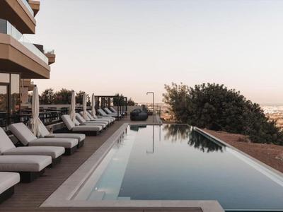 Piscina moderna con lettini, vista sulla città e alberi sullo sfondo.