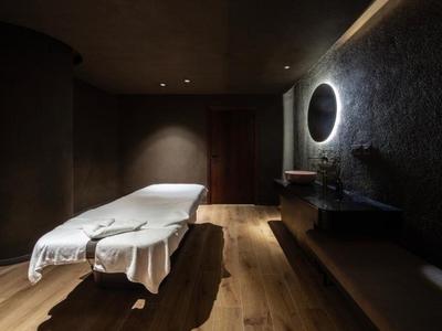 Ambiente spa oscurato con lettino da massaggio, specchio da parete e luce calda.