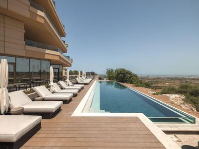Luxuriöser Hotelpool mit Liegestühlen und weitem Blick auf die Landschaft bei klarem Himmel.