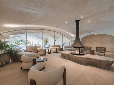 Ein modernes, helles Hotel-Lounge mit geschwungener Decke, Kamin und komfortablen Sitzgelegenheiten.
